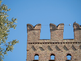 Medieval brick wall with merlons reaching for the blue sky in Busseto, Parma, Italy © august.columbo