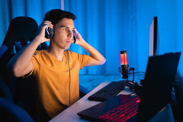 Gamer playing an online multiplayer game on a gaming laptop. He is adjusting the headset on his...