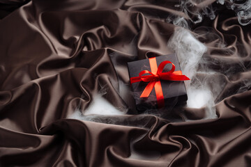 The gift, the concept of magic. A gift box with a red bow lies on a satin fabric with fog effect. Great for winter holidays or Valentine's day.