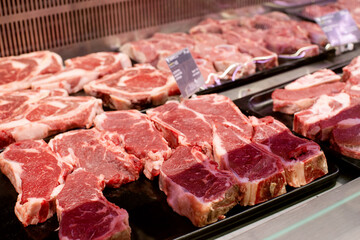 Raw beef and pork cuts of meat into steaks behind the glass of the refrigerator on the counter in the supermarket