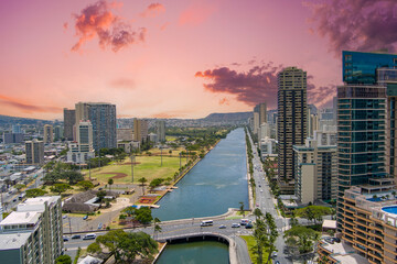Ala Wai Canal with skyscrapers, hotels and condos, lush green trees, cars on the street and...