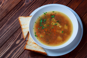 Vegetable soup with bread on wooden tray. White bowl on dark plank background. Top view. Copy space.