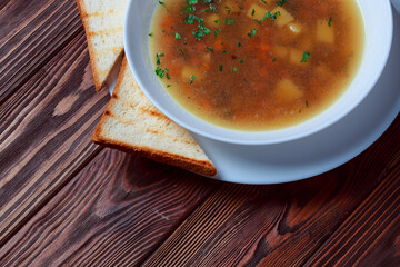 Vegetable soup with bread on wooden tray. White bowl on dark plank background. Top view. Copy space.