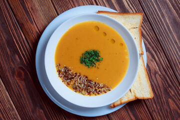 Vegetable soup with bread on wooden tray. White bowl on dark plank background. Top view. Copy space.