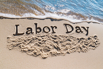 Fototapeta premium The words Labor Day written in the sand on a beach, with water waves