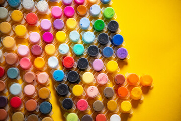 Collection of small jars filled with vibrant acrylic paints in a variety of colors and shades on a bright yellow background. 