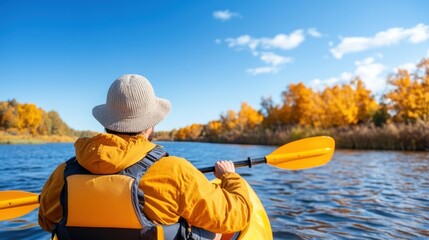 An individual enjoys kayaking on a serene river, surrounded by colorful autumn trees. The bright blue sky adds to the peaceful outdoor experience during a sunny day