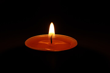 Single candle burning in darkness. Orange flame