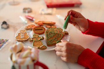 Lady making homemade Christmas cookies, decorating gingerbread tree with green icing, closeup shot