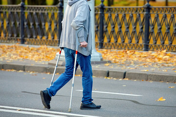 Man with crutches navigating road crossing, violation of pedestrian safety regulations. Man crossing the road on crutches, violation of pedestrian safety rules in an urban environment.