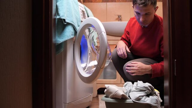 Sad man looking at broken washing machine in bathroom