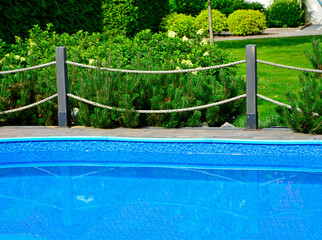 błekitna woda w ogrodowym basenie otoczonym drewnianym płotkiem i sznurami, blue water in the garden swimming pool with a fence and ropes	
