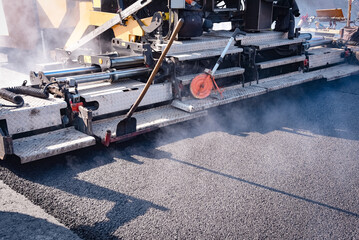 Strassenbau - Asphaltfertiger legt einen neuen Fahrbahnbelag aus heissem Asphalt, Praxisfoto -...