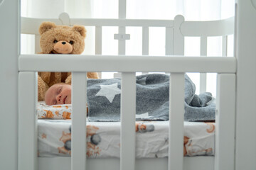 newborn baby sleeping in a bed. Infant lying in baby crib covered with blanket. Teddy bear is a...