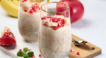 A glass of chia seeds and yogurt, with banana pieces and pomegranate seeds added to the dessert