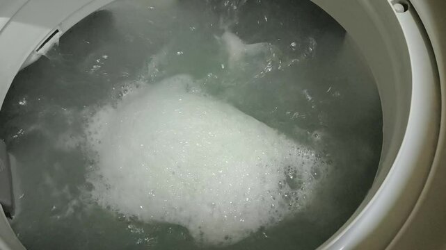 Dirty clothes spinning in a top-loading washing machine. Laundry and house keeping concept