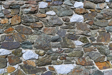 A close-up view of a rustic stone wall composed of variously shaped and colored rocks, showcasing a rugged and textured surface with natural hues, ideal for backgrounds or architectural references.