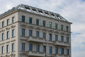 Elegant building with neoclassical architectural elements and large windows, featuring balconies and ornate details under a cloudy sky. Urban architecture, modern construction and exterior design