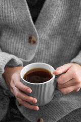Woman in grey cozy sweater holding mug with espresso coffee close up.