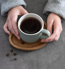 Woman in cozy sweater holding mug with espresso coffee close up on a gray table.
