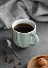 Espresso coffee in a mug on a wooden board on a dark background with coffee beans, cookies, spoon and a cozy gray sweater.