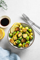 Fried brussels sprouts in a bowl with soy sauce, lemon and sesame on a light background with  herb and napkin.