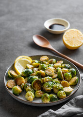 Crispy brussels sprouts in a plate with soy or balsamic sauce and sesame on a dark  background with spoon and lemon.