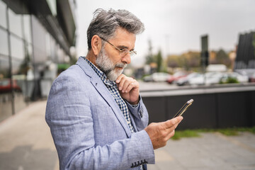 senior concentrated man use mobile phone in front modern company