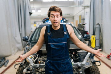 Portrait of puzzled mechanic male shrugging shoulders while not knowing what disrepair with repair car. Doubtful repairman wearing workwear clothes, trying to solve problem. Concept of car service.