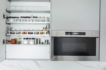 Smart kitchen organization. Lots of storage jars with various seeds and spices on shelves in kitchen interior near built-in microwave oven