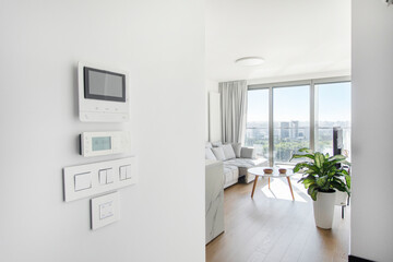 Light switches, air conditioner remote control and modern telecom display on white wall with living room on background copy space