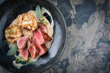 Roasted saddle of venison fillet with bread dumplings in a creamy mushroom sauce served as a top view in a design bowl with copy space right