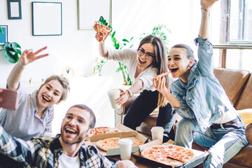 Friends laughing and taking selfie on smartphone with two fingers while eating pizza