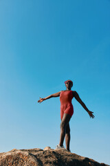 Obraz premium Woman in red swimsuit standing on a rock against a clear blue sky
