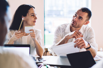 Confident colleagues having conversation and holding papers during meeting