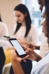Ethnic businesswoman surfing smartphone and standing with coworkers at work