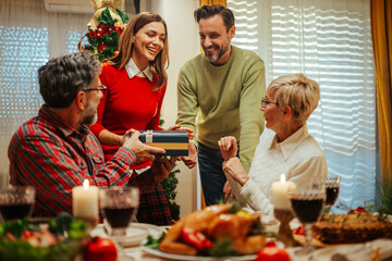 Happy family exchanging christmas gifts at dinner table