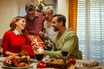 Fototapeta premium Happy family having christmas dinner exchanging gifts