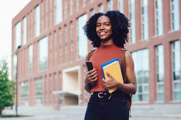 Smiling black lady with cellphone and books in hand