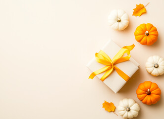 Obraz premium A beautifully wrapped white gift box adorned with a bright yellow ribbon, surrounded by small decorative pumpkins in orange and white.