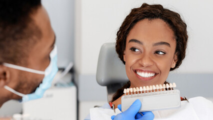 Dentist applying tooth scale samples set to smiling black lady patient of dental clinic, close up