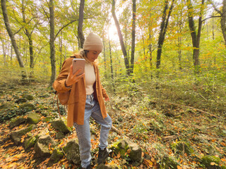 A woman is walking in a forest with a cell phone in her hand