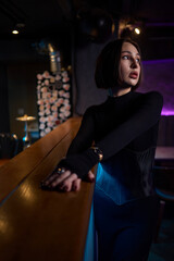 An Elegant Model Dressed in a Chic Black Outfit Poses at a Modern Bar Setting for Photography