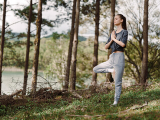 Calm young woman practicing yoga in a serene forest, balancing on one leg with hands in prayer position, surrounded by greenery and tranquil nature