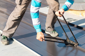 Roofer assembles sheet metal on the roof. Construction workers - installation assembly of new roof. Roofing tools.