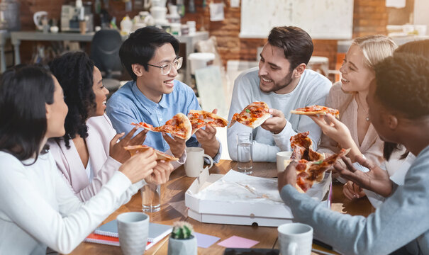 Friendly international business team enjoying pizza together in office