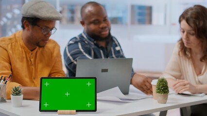 Clients negotiating with realtor next to isolated copy space on tablet, examining layout and blueprints for new high class office space. Business people investing in property with financier. Camera B.