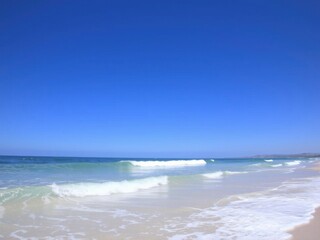 Fototapeta premium Soft blue ocean wave gently washing up onto a pristine sandy beach, travel, sand