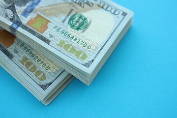 Big amount of hundred dollar bills in thick stack lies on bright blue color paper background