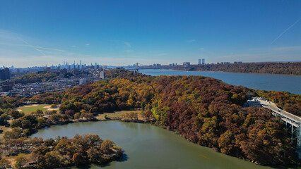 Obraz premium This location in the Bronx offers stunning views of lush greenery, a picturesque lake, and urban structures. Framed by the river, it showcases iconic bridges and the New York City skyline in the dista